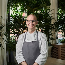 Executive Pastry Chef Kalen Hendrick standing in an upscale setting in a white chef’s coat.